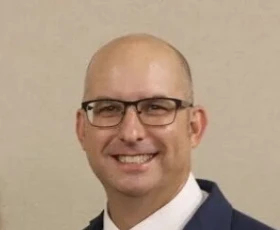 El pastor Dodd, sonriendo, con lentes y traje azul marino